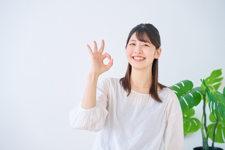 白いブラウスの女性が笑顔でOKサインをしている様子